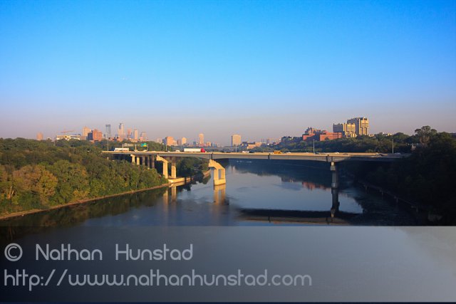 Downtown Minneapolis and the University of Minnesota campus during rush hour from the Franklin Avenue Bridge. The Interstate 94 bridge across the river can be seen.